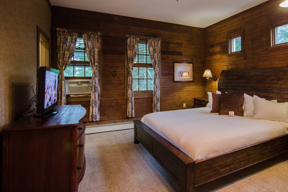 A wooden-paneled bedroom with a large bed, two bedside lamps, a dresser, and a television on a wooden cabinet.