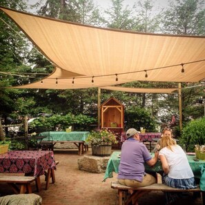 An outdoor patio area with tables and benches, a wooden structure, and string lights.