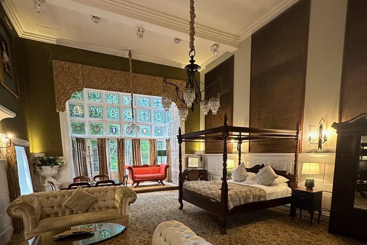 Um quarto espaçoso com uma cama grande, um sofá, uma mesa de centro de vidro e um lustre.