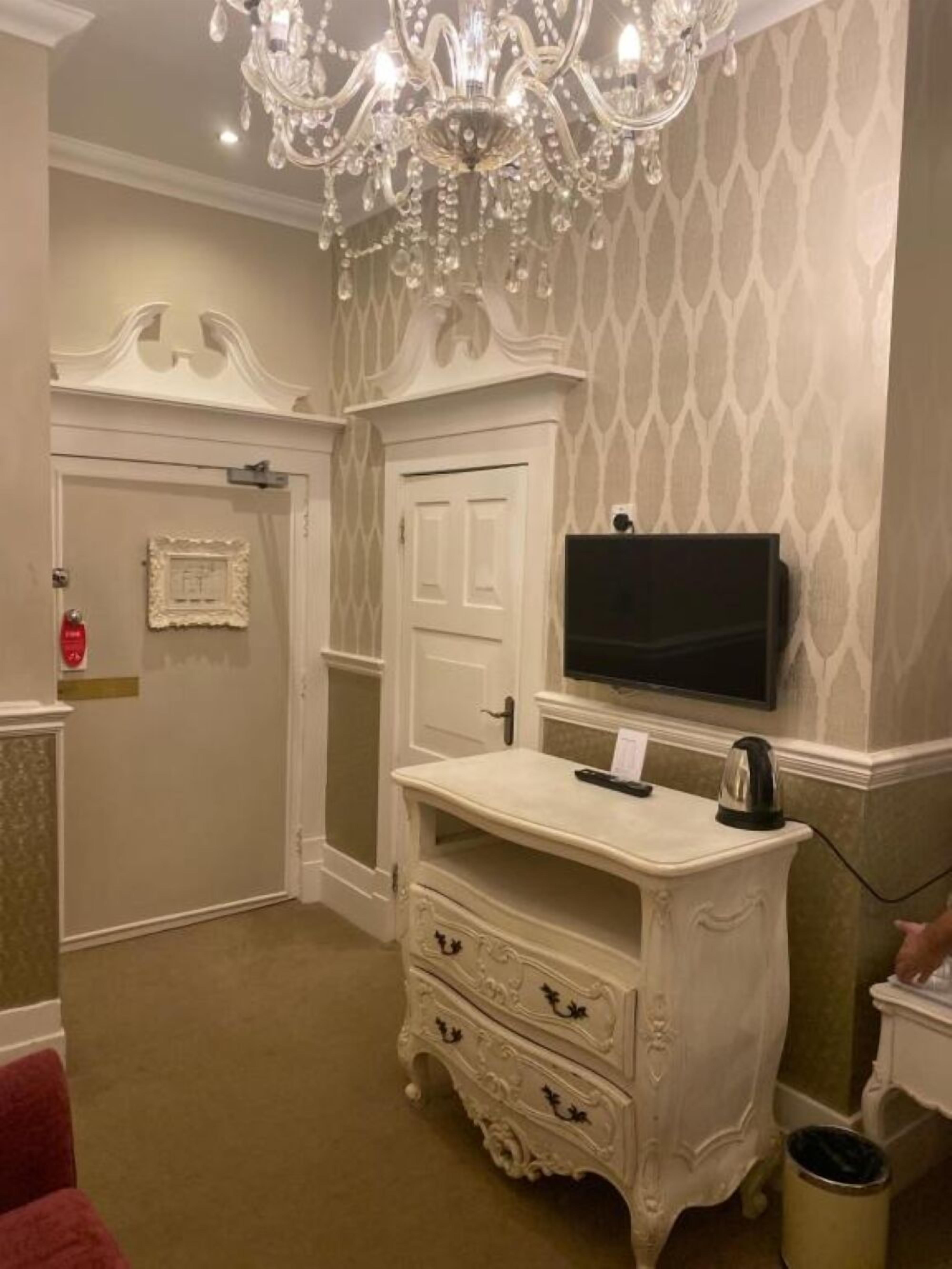 A room with a white ornate dresser, a television, and a chandelier.