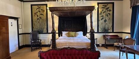 A spacious bedroom with a four-poster bed, a red upholstered sofa, and a chandelier.