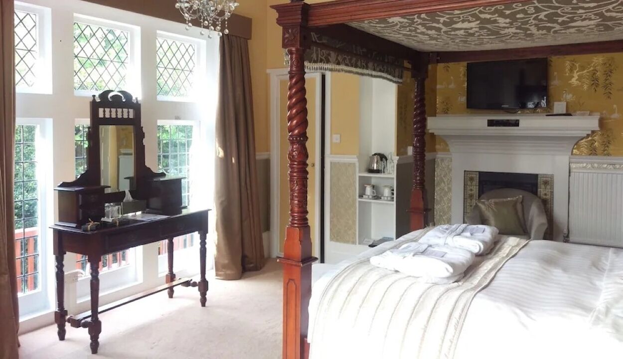 A bedroom with a four-poster bed, a dresser, a mirror, and a fireplace.