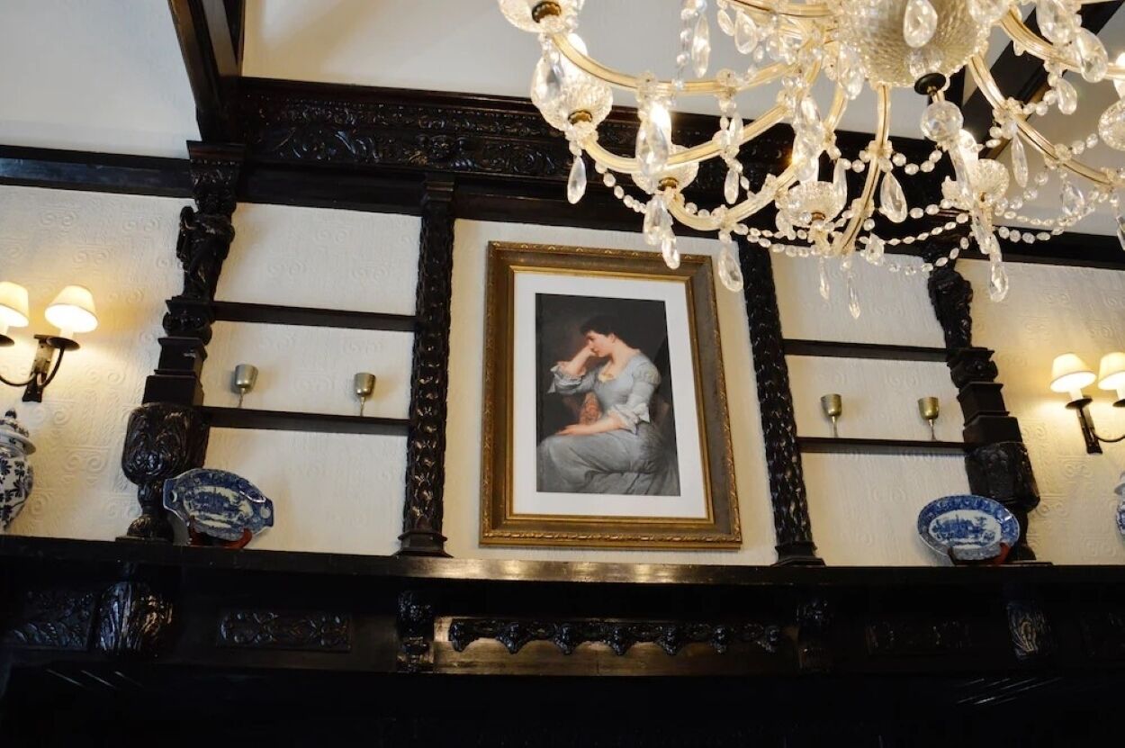 A framed portrait on a wall with a chandelier above.