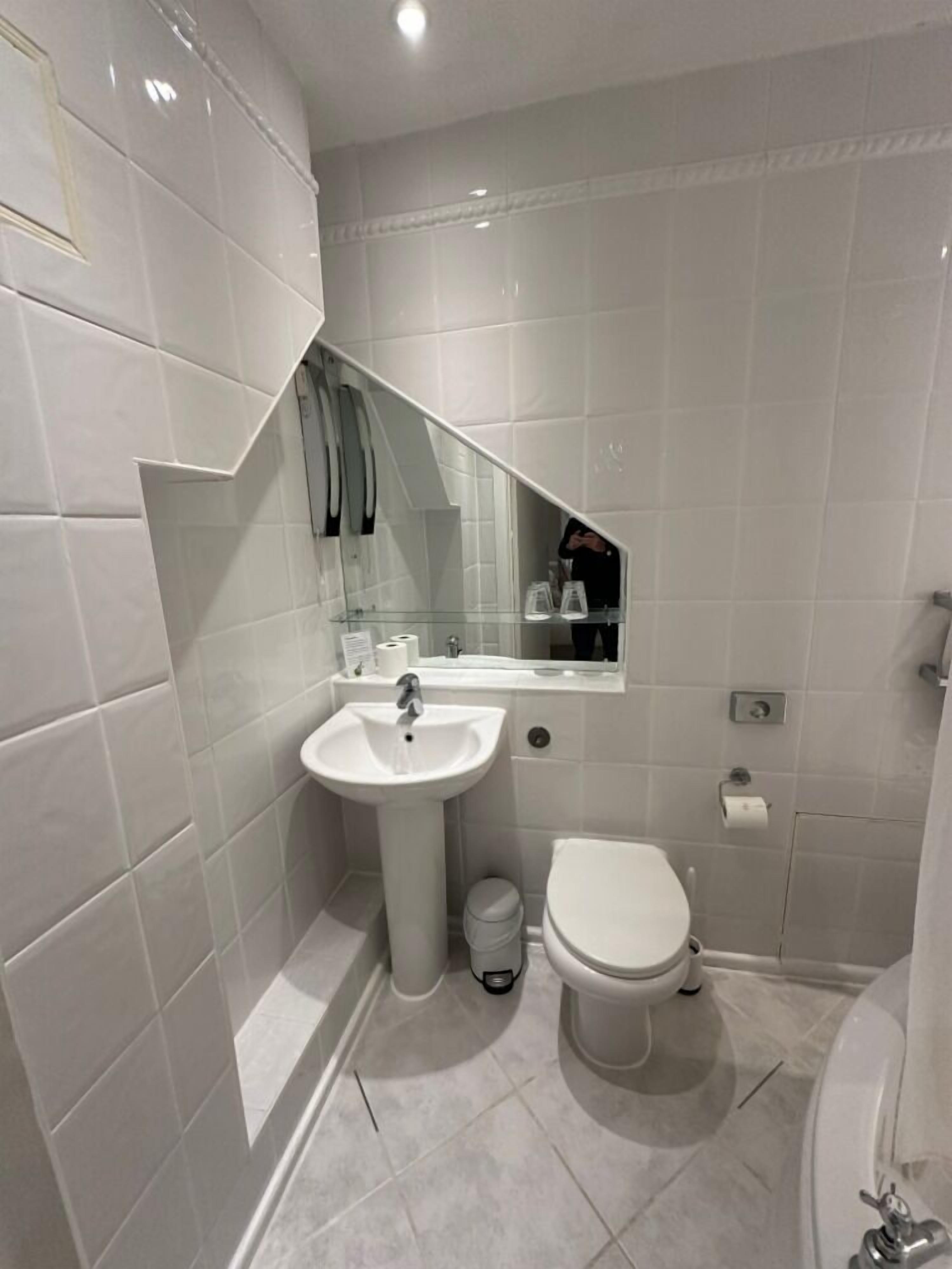 A modern bathroom with white tiles, a sink, toilet, and a bathtub.