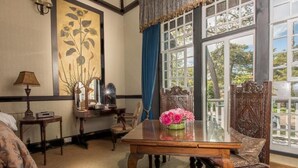 Una habitación con una mesa de madera, una silla, una lámpara, un cuadro y una ventana con cortinas.