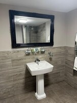 Un baño con un lavamanos blanco de pedestal, un espejo grande con marco negro y revestimiento de madera en las paredes.
