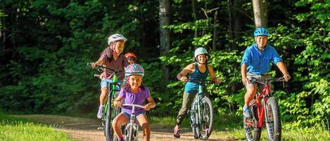 A group of people riding bicycles on a dirt path surrounded by trees.