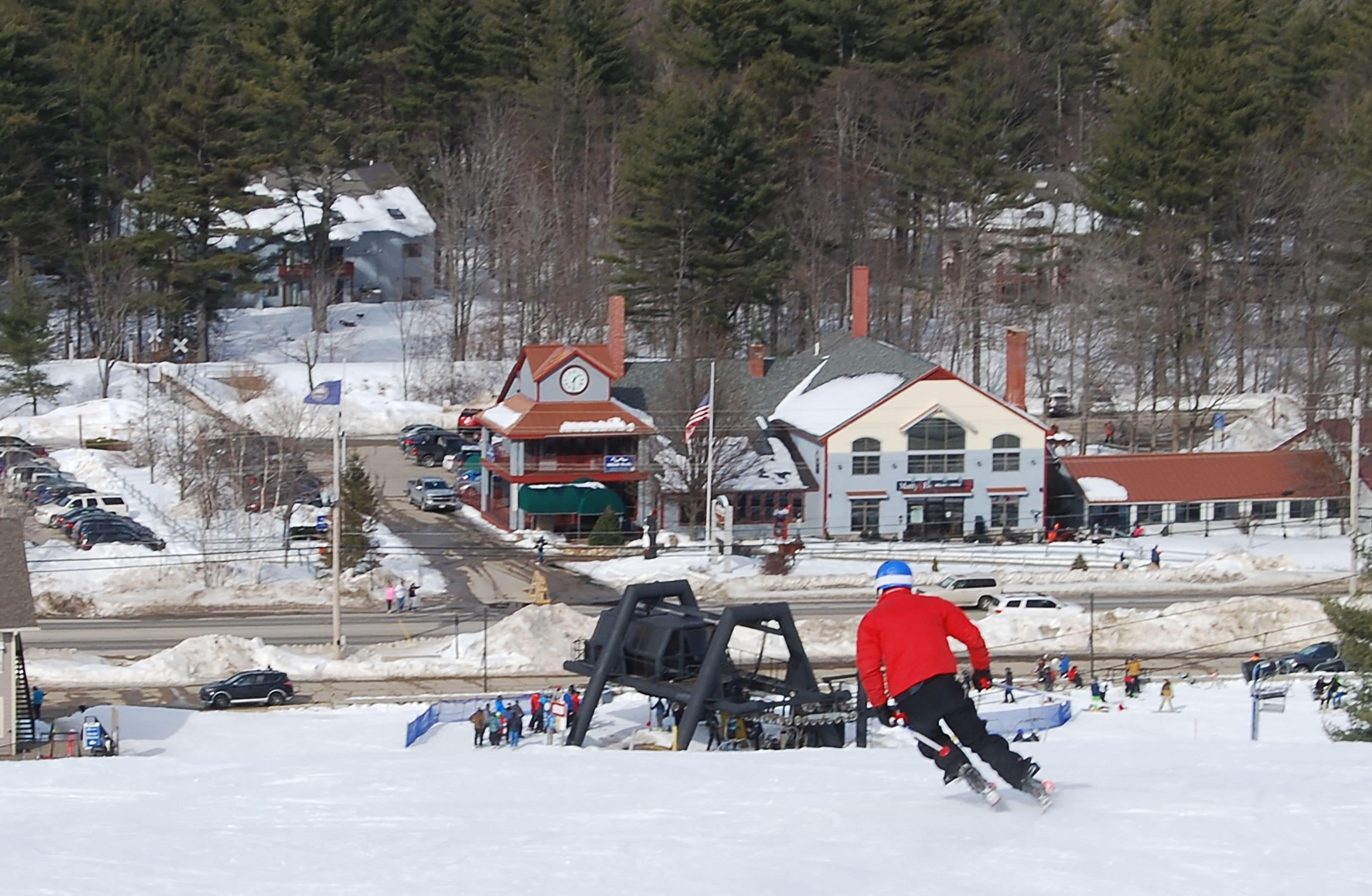 A snowy landscape with a ski lift, buildings, and a person skiing.