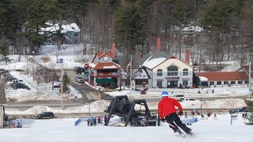 A snowy landscape with a ski lift, buildings, and a person skiing.