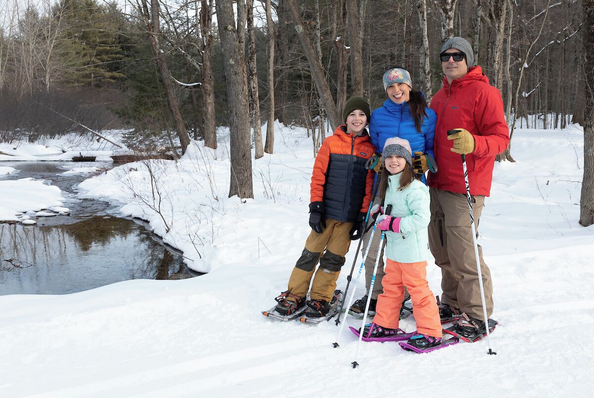 Una familia esquiando cerca de un arroyo cubierto de nieve en un bosque.
