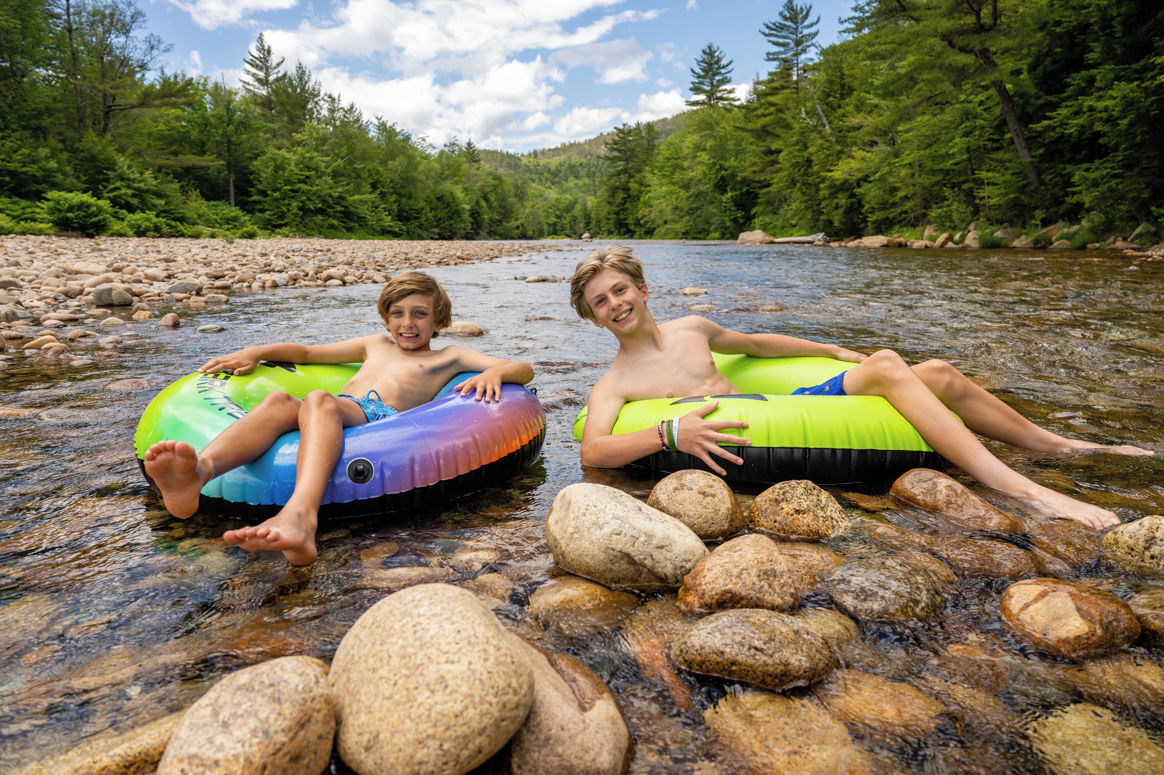 Dos personas descansando en flotadores en un río rodeado de rocas y árboles.