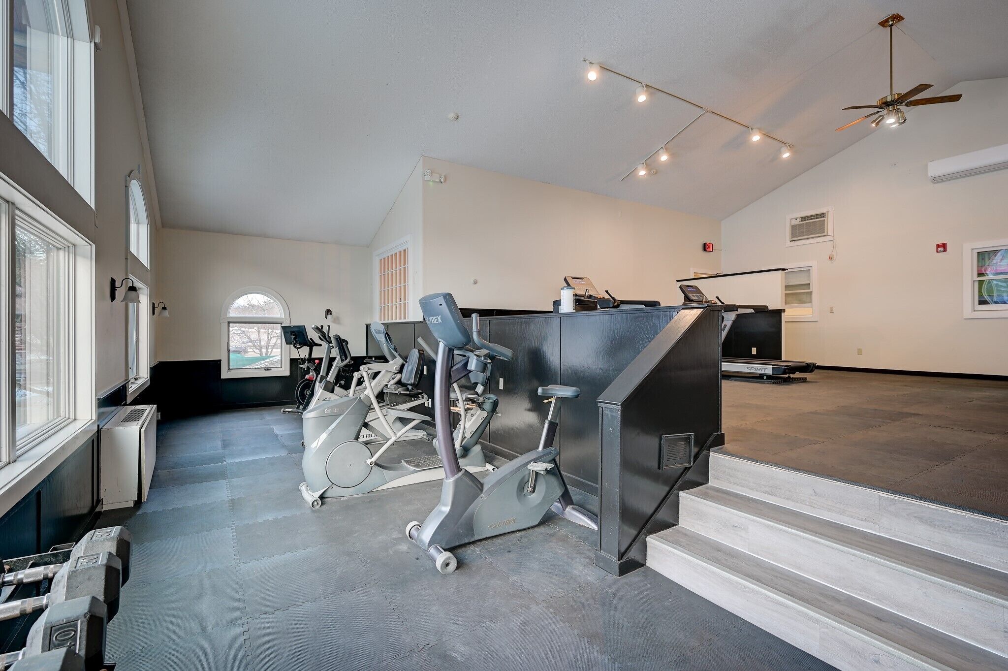 Ein geräumiger Fitnessraum mit verschiedenen Trainingsgeräten, darunter Laufbänder und Ergometer, sowie ein großes Fenster, das für natürliches Licht sorgt.