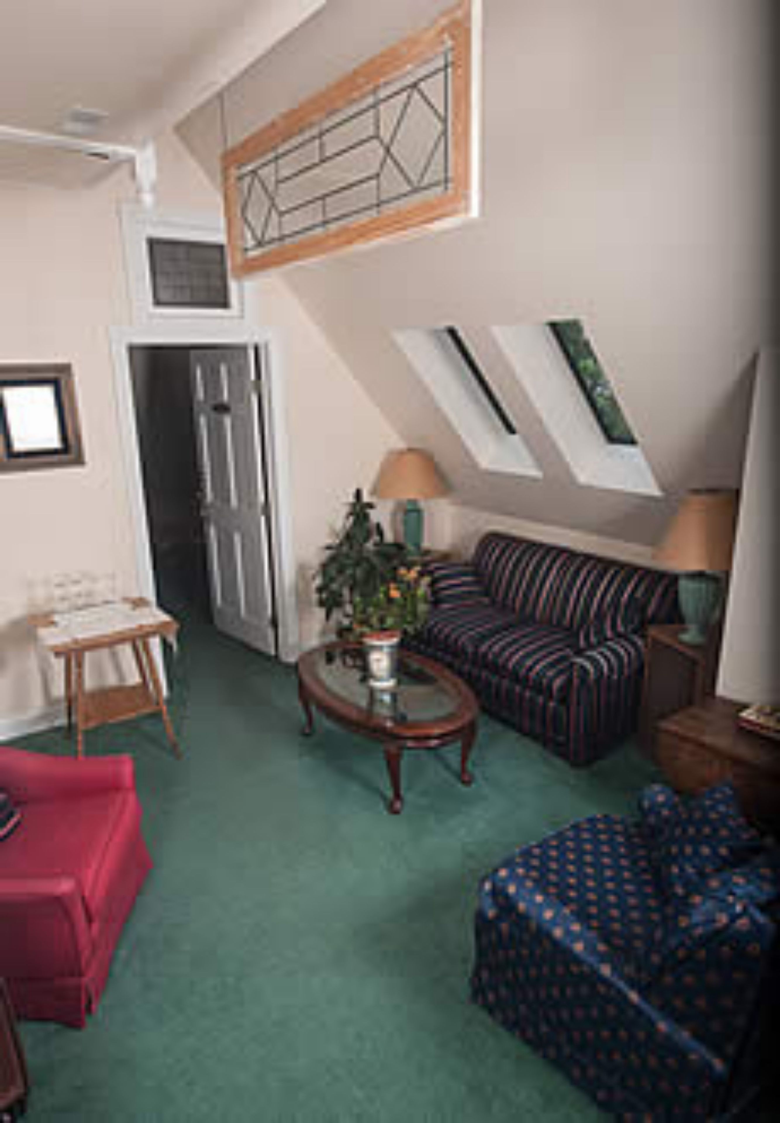 A compact living space with a sofa, a red chair, a coffee table, and a small table with a lamp. There is a window with a view of the outside.