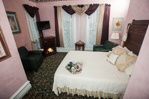 A hotel room with a bed, a fireplace, a television, a green armchair, and a small table with a tray of items.