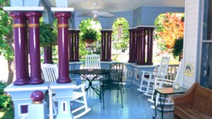 A covered porch with a blue floor, white rocking chairs, a wooden bench, and purple columns. - Market Street Inn (Taylorville)