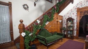 A staircase with a green velvet sofa at the bottom, a wooden railing, and a floral wallpapered wall. - Market Street Inn (Taylorville)