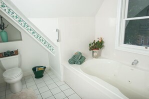 A bathroom with a white bathtub, a toilet, a green bucket, and a small potted plant.