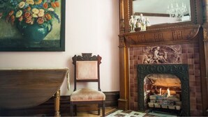 A room with a wooden chair, a fireplace with a mirror above it, and a painting of flowers on the wall. - Market Street Inn (Taylorville)