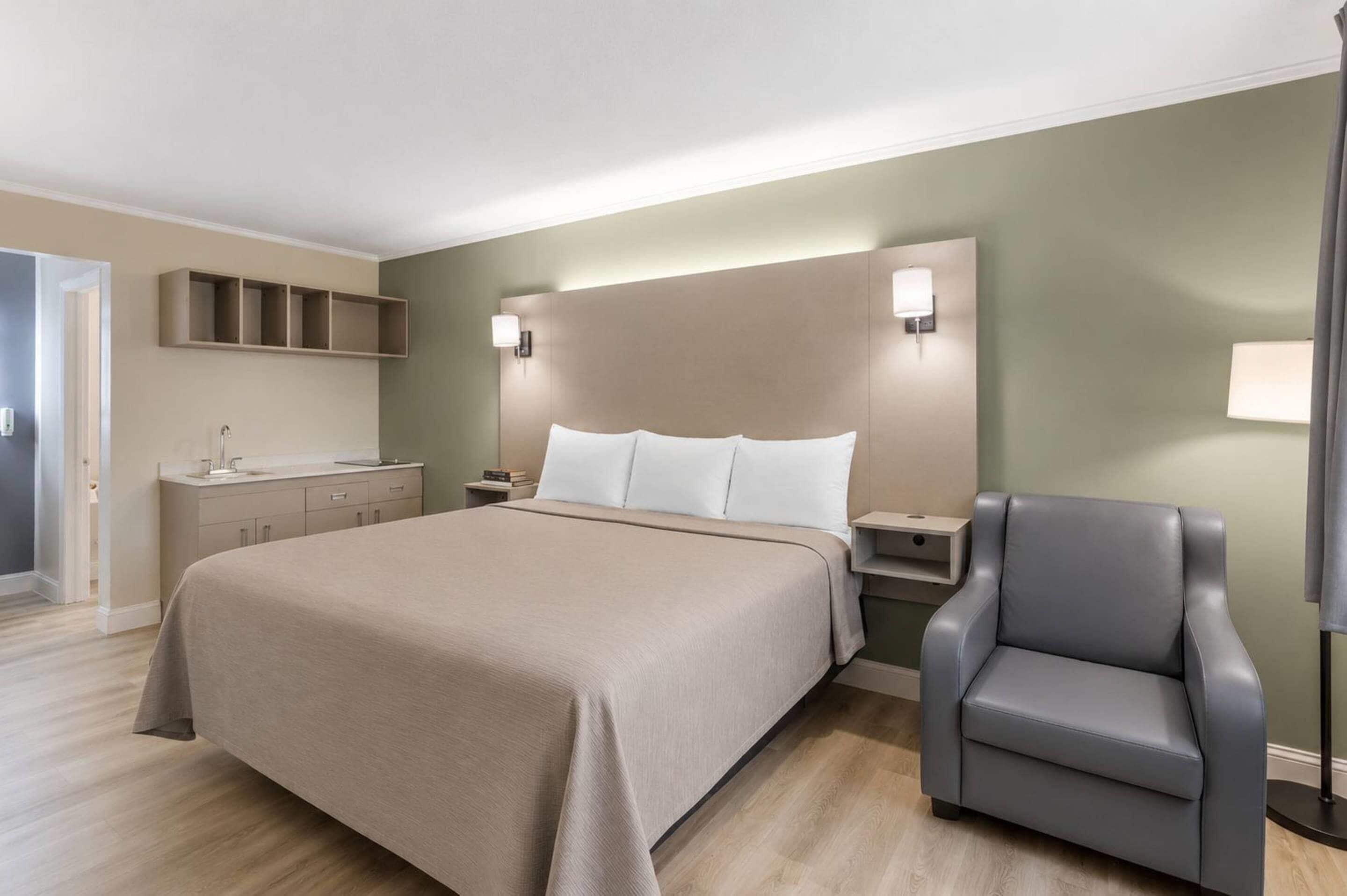 Una habitación de hotel con una cama, mesitas de noche, una silla y un estante en la pared.