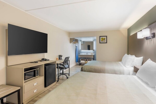 A hotel room with a bed, a desk with a computer, a microwave, and a TV.