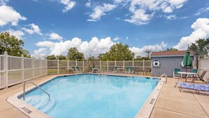 A rectangular swimming pool with a no diving sign, surrounded by a white fence, and adjacent to a small building with a green umbrella. - Quality inn Lancaster (Lancaster)