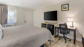 Quarto de hotel com uma cama grande, uma escrivaninha com computador, televisão e uma luminária.