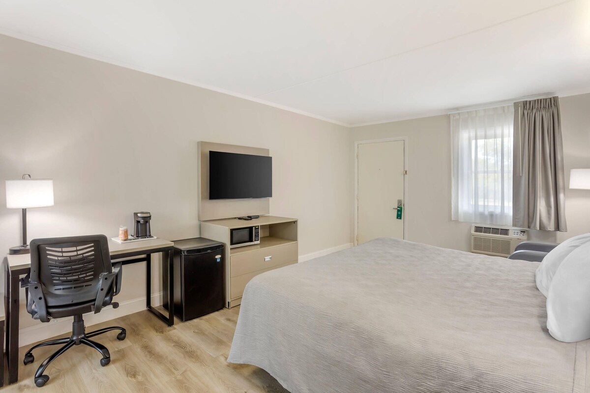 A hotel room with a bed, desk, chair, TV, and a small kitchenette.