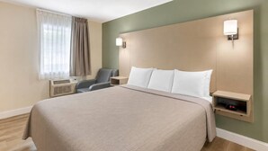 A hotel room with a large bed, a chair, a nightstand with a clock, and a wall-mounted lamp. - Quality inn Lancaster (Lancaster)