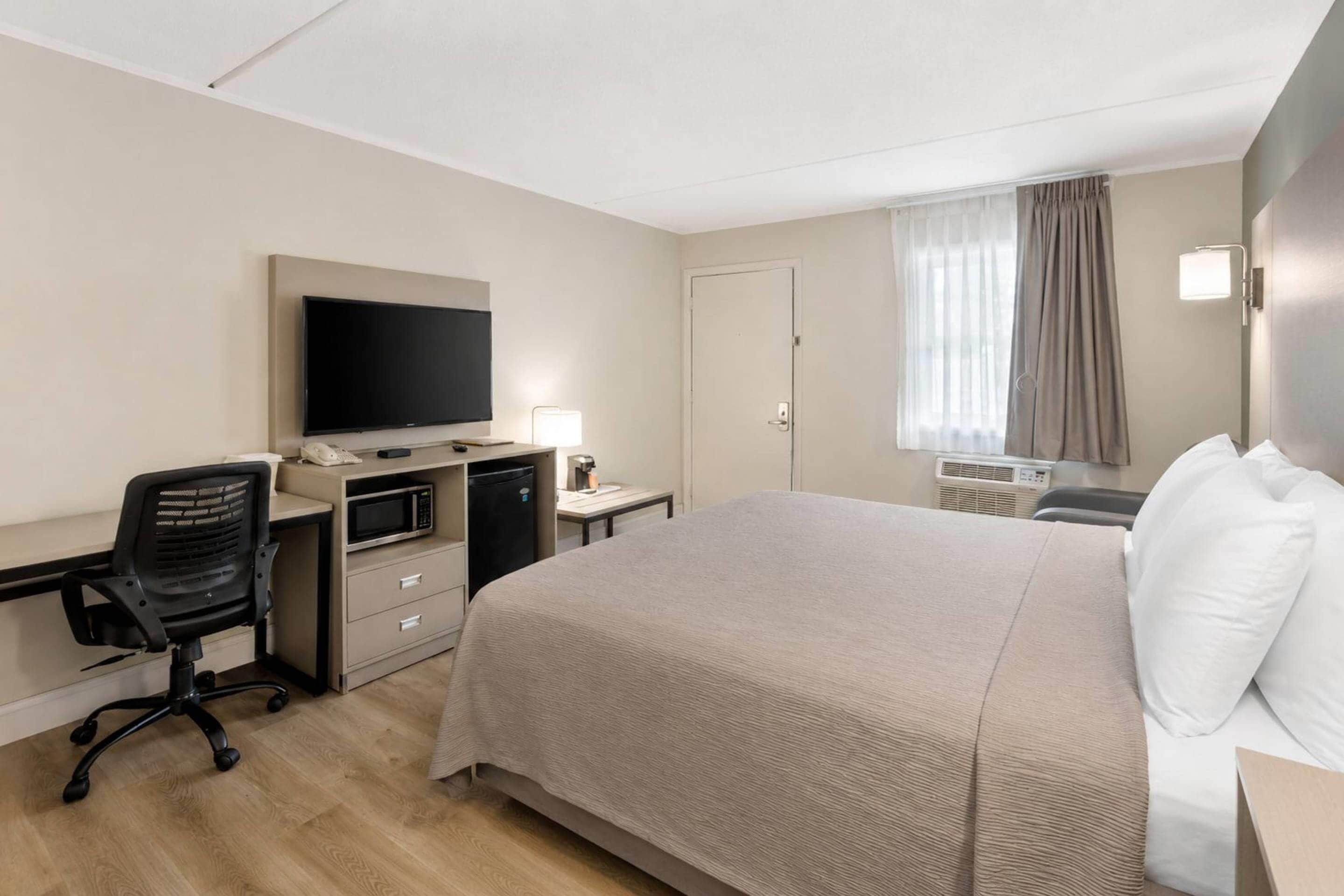 A hotel room with a bed, desk, chair, television, and a window with curtains.