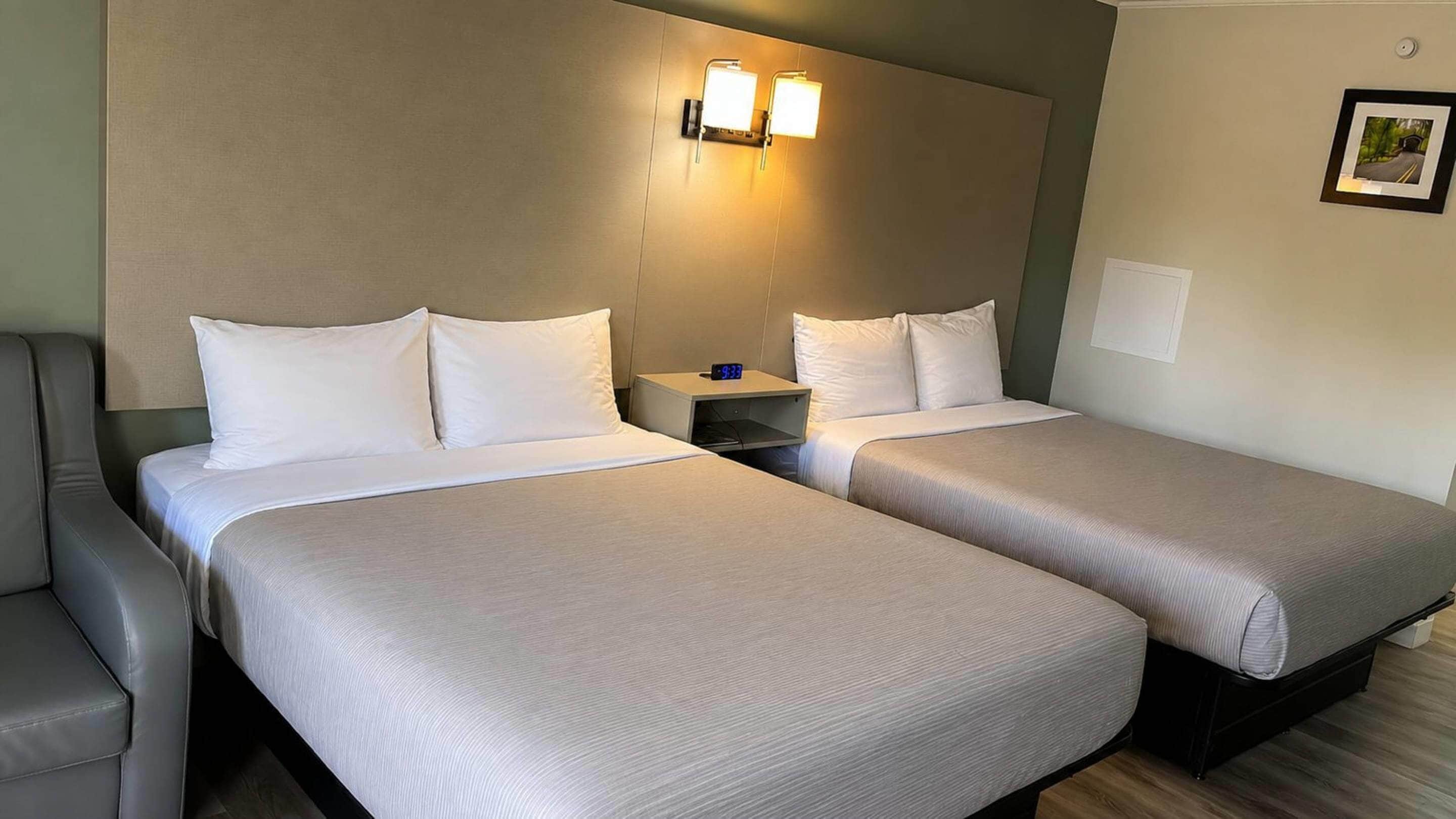 Een hotelkamer met twee bedden, een nachtkastje met een klok en een lijst aan de muur.