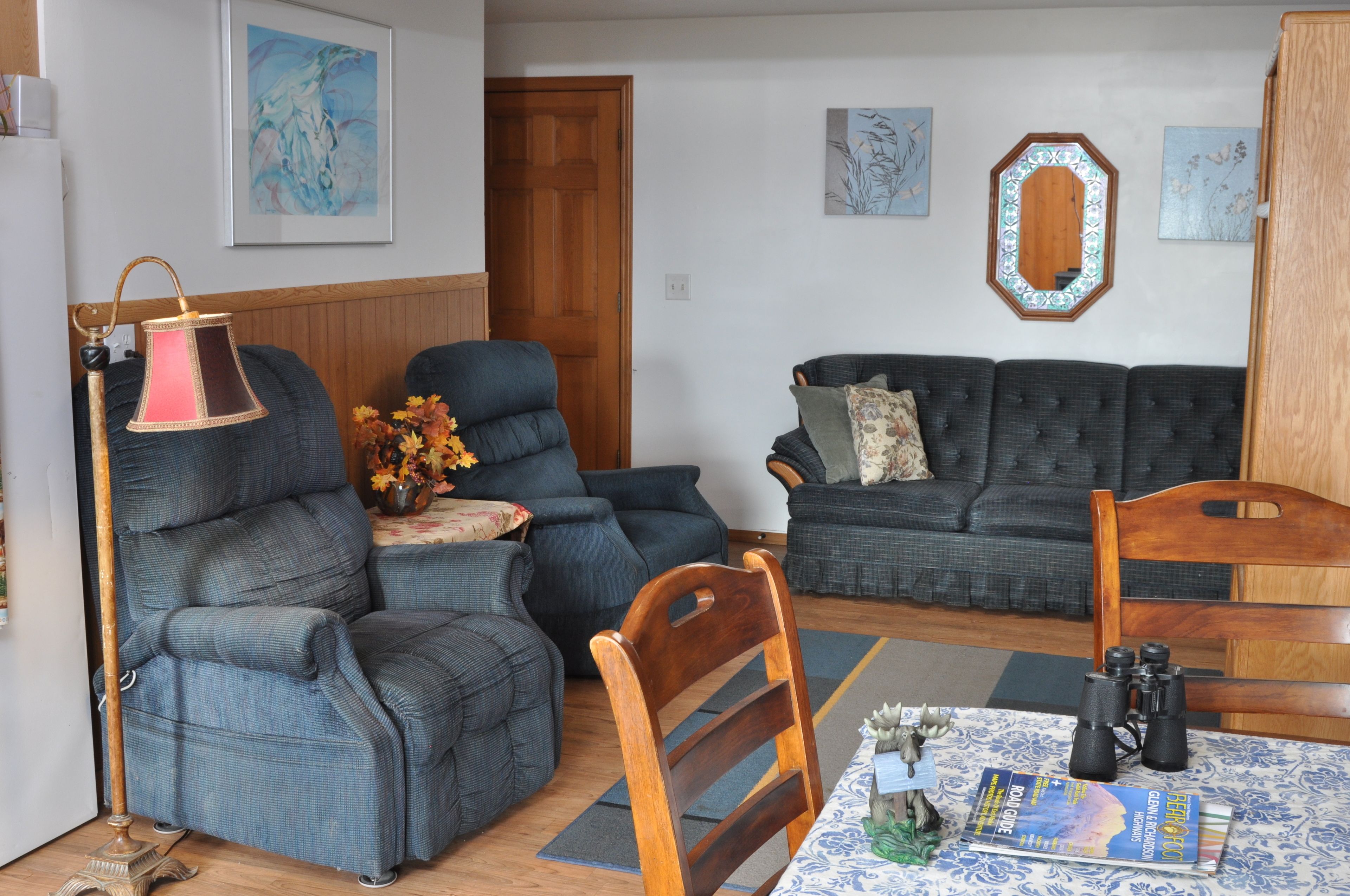 A living room with two sofas, a wooden chair, a table with a magazine, and a lamp.