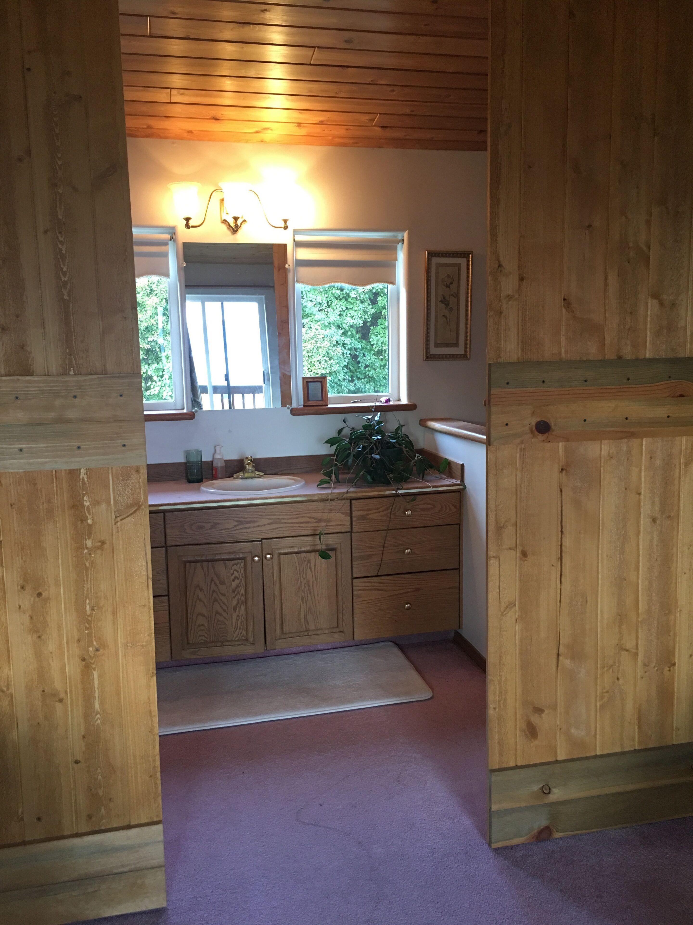 A wooden interior with a kitchen area, including cabinets, a sink, and a window with a view of greenery.
