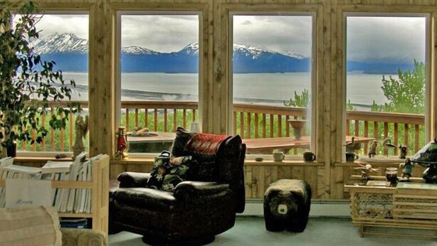 A cozy room with a view of a lake and mountains, featuring a wooden deck, a leather armchair, and a small ottoman. - Majestic View B&B (Homer)