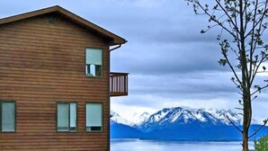 A wooden building with a balcony, overlooking a lake and snow-capped mountains. - Majestic View B&B (Homer)