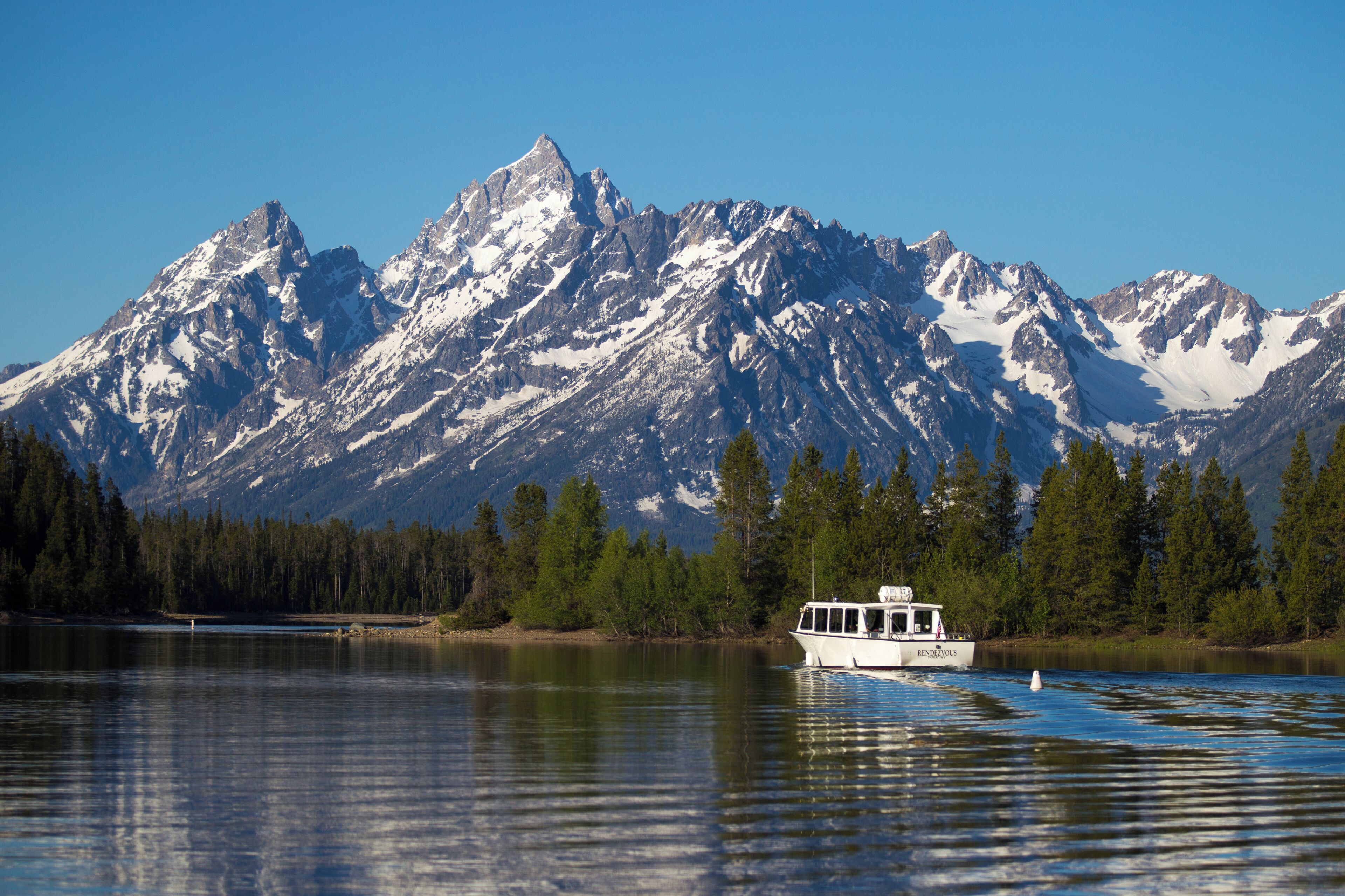 Um barco num lago calmo, com montanhas cobertas de neve ao fundo.