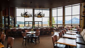 A restaurant with a bar area, multiple tables and chairs, and large windows offering mountain views.