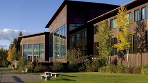 A modern building with large windows and a grassy area with benches.