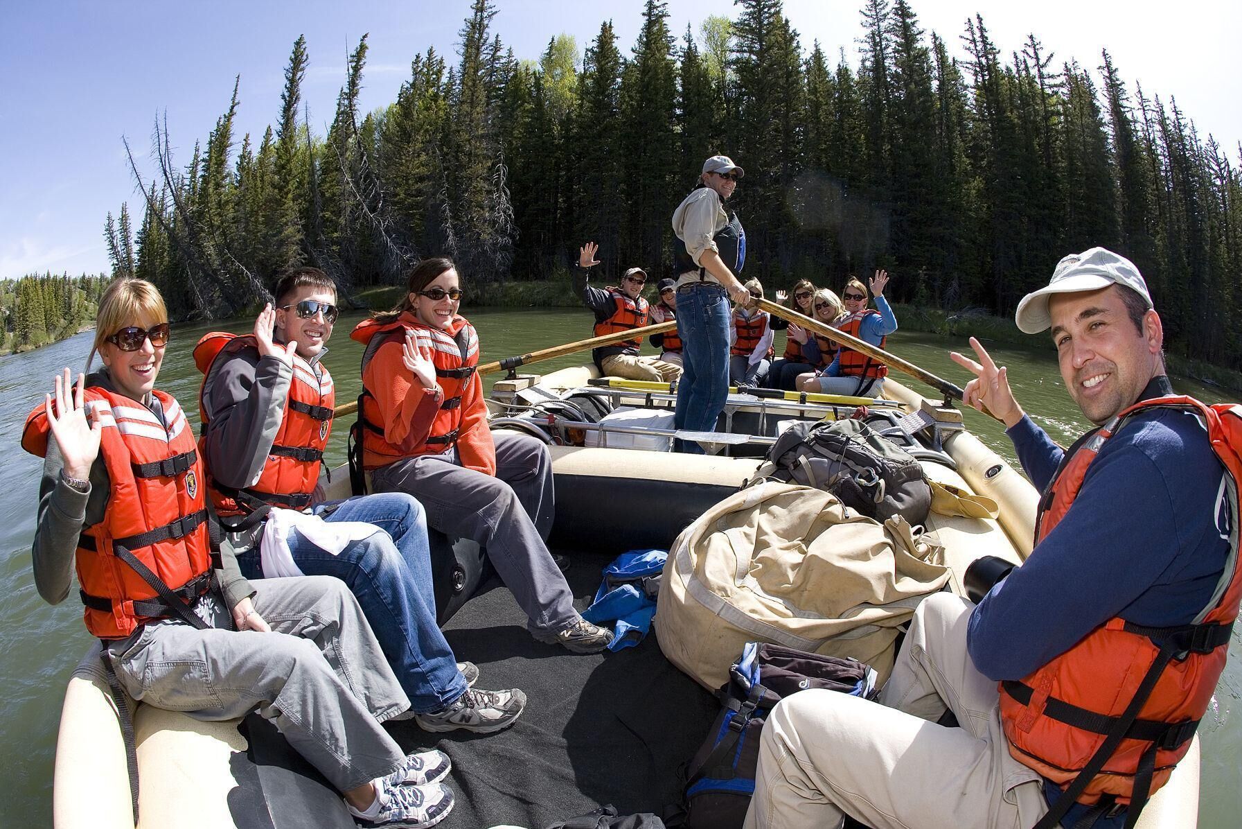 A group of people on a boat with life jackets, surrounded by a forested area.