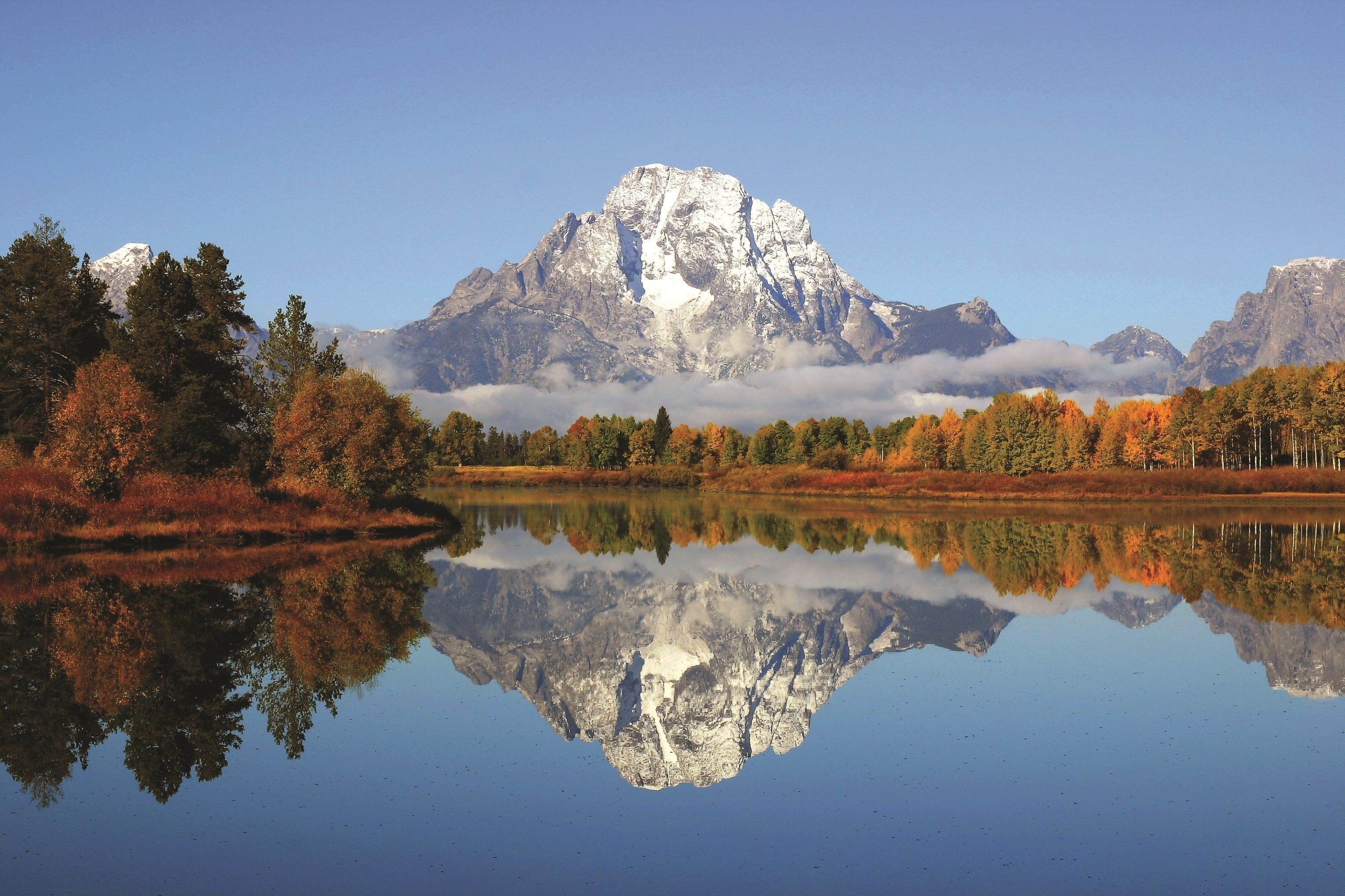 A mountain reflected in a calm lake with autumn foliage.