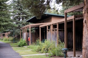 Una hilera de cabañas con fachada de madera y porches cubiertos, rodeadas de follaje y árboles.
