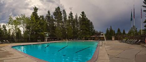 A swimming pool with a diving board, surrounded by lounge chairs and a wooden deck.