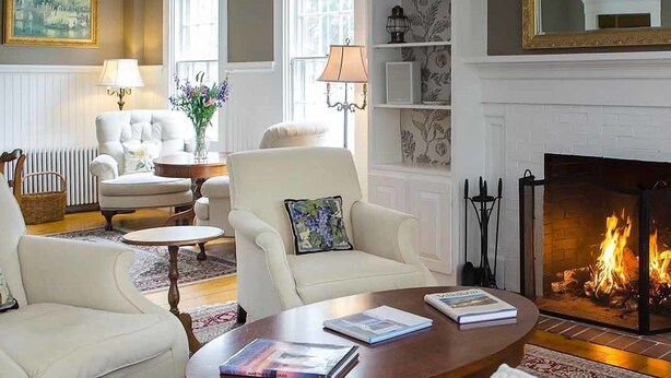 A cozy living room with a fireplace, comfortable seating, and a bookshelf. - The Ashley Inn (Edgartown)
