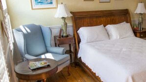 A hotel room with a large bed, a chair, a small table with a lamp, and a dresser. - The Ashley Inn (Edgartown)