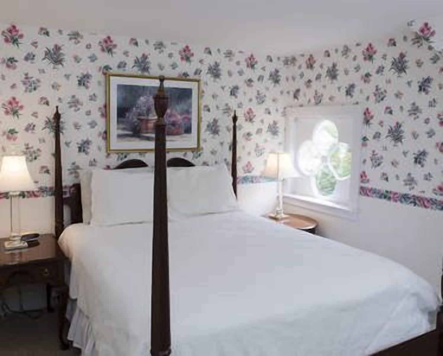 Una camera da letto con un letto a baldacchino, carta da parati a motivi floreali, un quadro appeso al muro e due comodini con lampade.