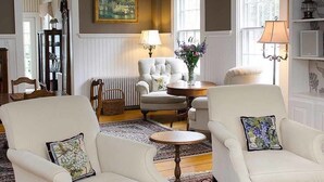 A cozy living room with two white armchairs, a round table, a fireplace, and a bookshelf. - The Ashley Inn (Edgartown)