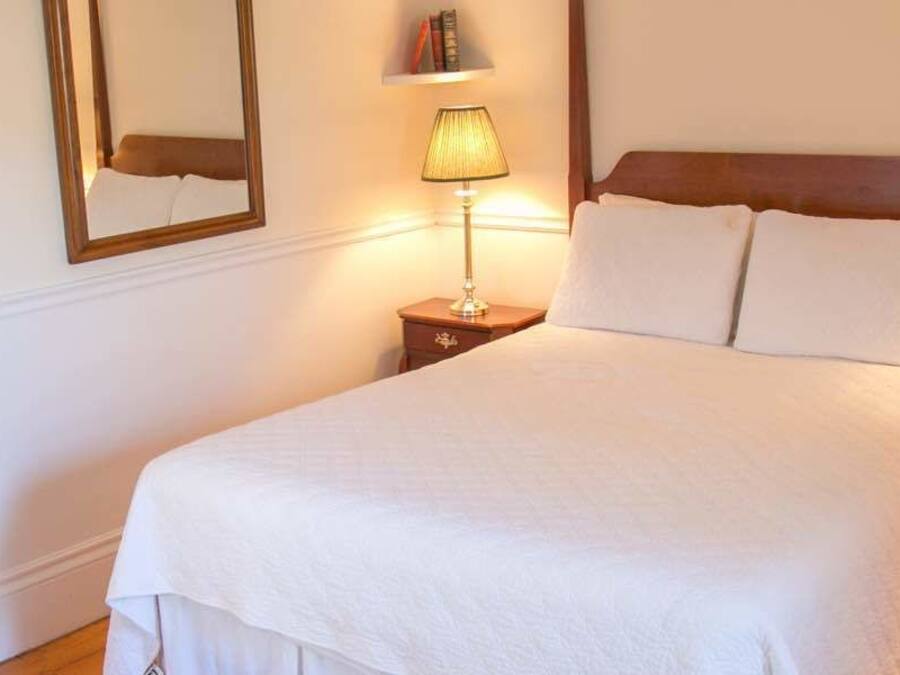 A neatly made bed with white linens, two bedside lamps, and a wooden headboard.