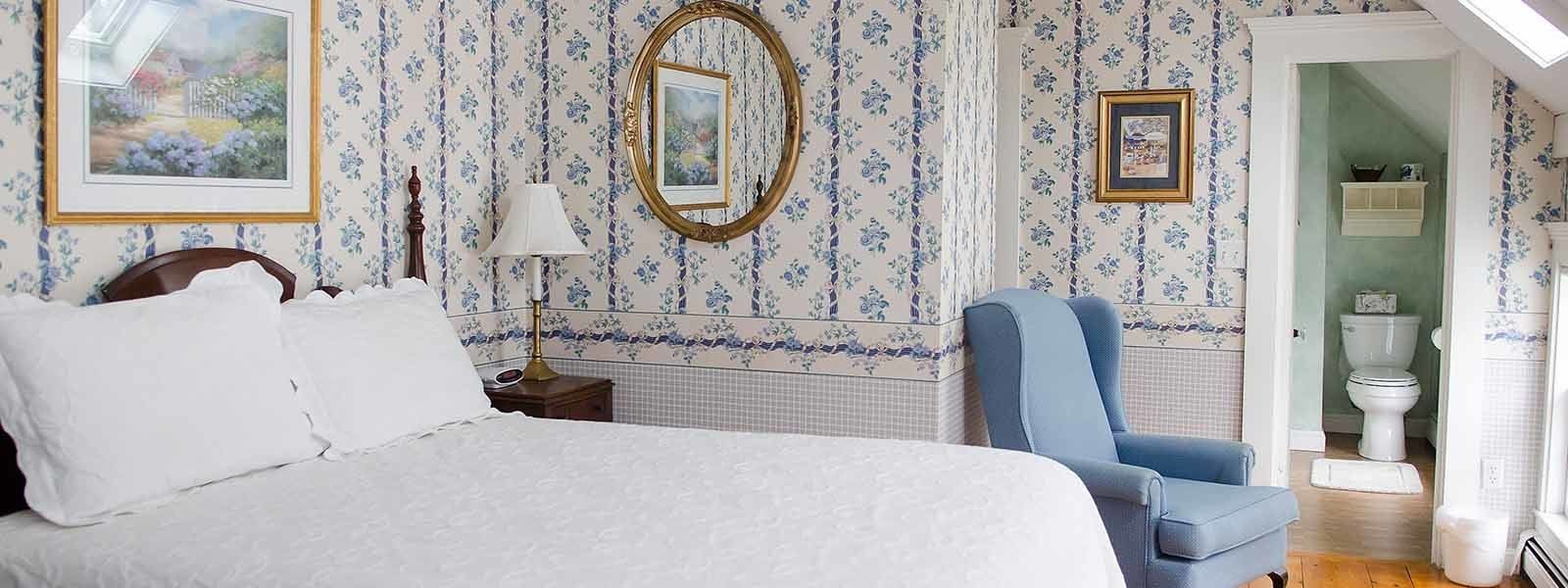 A bedroom with a large bed, a blue armchair, and floral wallpaper.