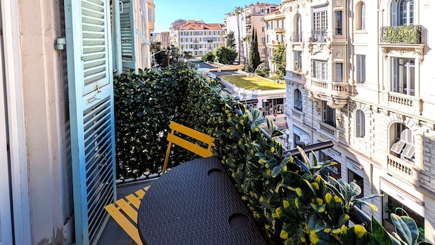 A balcony with a table and chairs, overlooking a street with historic buildings. - H33 hôtel (Nice)