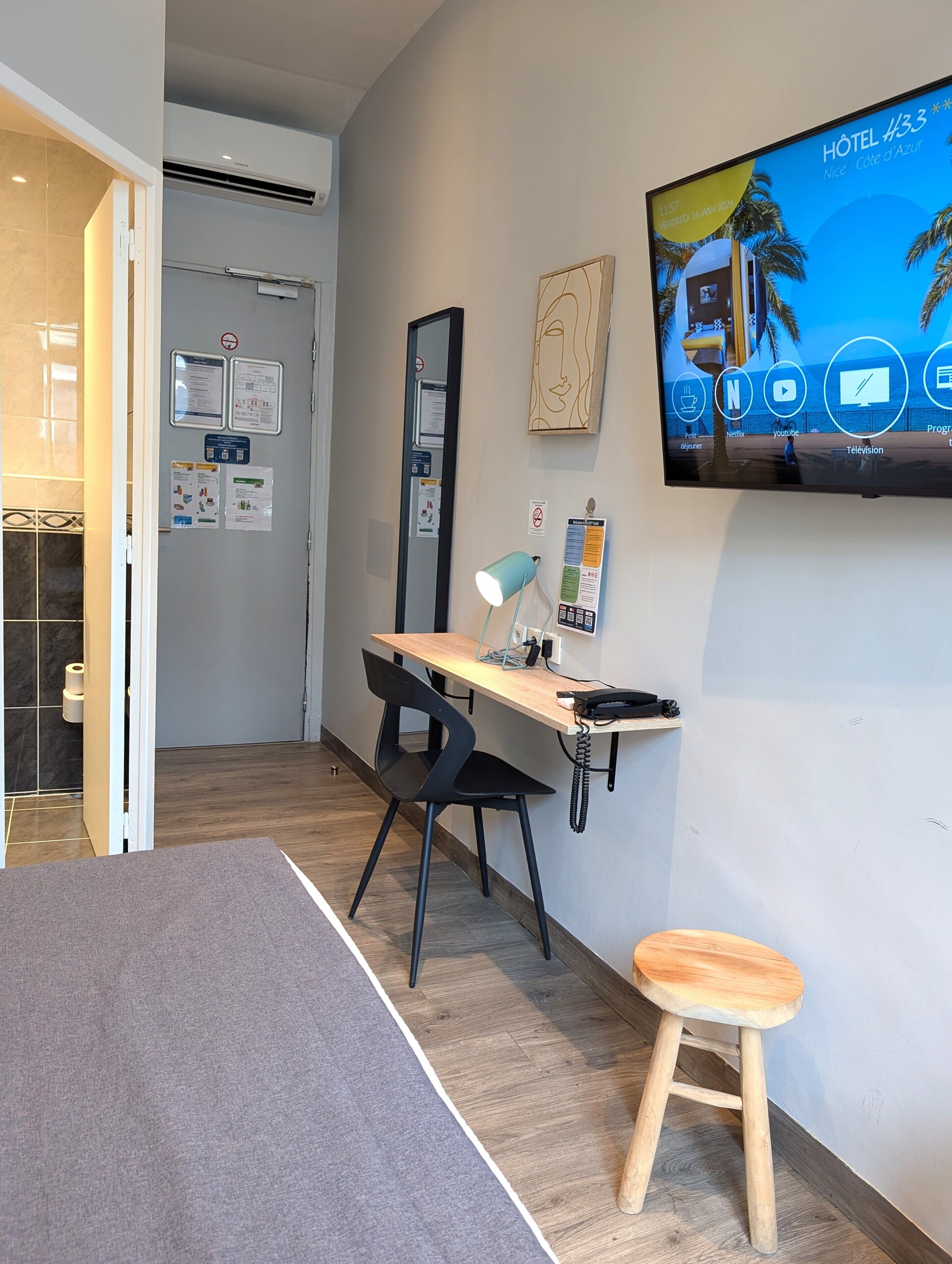 A modern hotel room with a desk, chair, and a television displaying the hotel's name and amenities.
