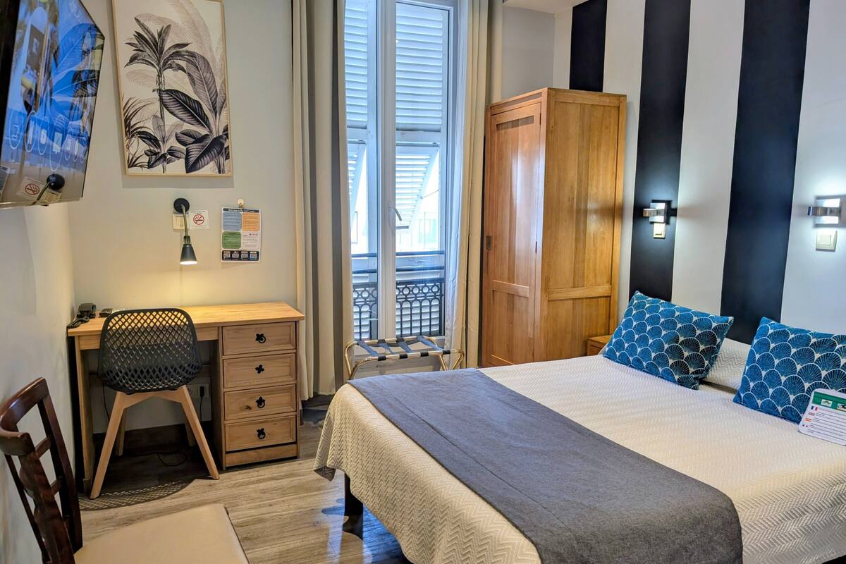 A bedroom with a bed, a desk, a chair, a wardrobe, and a window with a view.